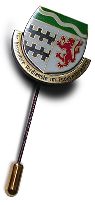 Ehrennadel des Feuerwehrverbands Rheinisch-Bergisch Kreis Ein Abzeichen in Form eines Wappens mit grünem und silberfarbenem Design. Es zeigt einen roten Löwen und grafische Muster. Unter dem Wappen steht der Schriftzug "Für besondere Verdienste im Feuerwehrwesen". Das Abzeichen hat eine Nadel für das Anstecken.